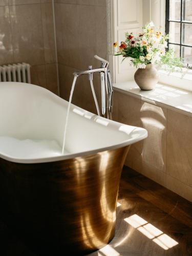 a bath tub in a bathroom with a vase of flowers at Rhinefield House Hotel in Brockenhurst