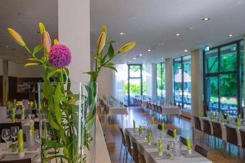 un vaso con un fiore viola in una stanza con tavoli di Heideblick - Tagungs- und Freizeithotel an der Lüneburger Heide a Jesteburg