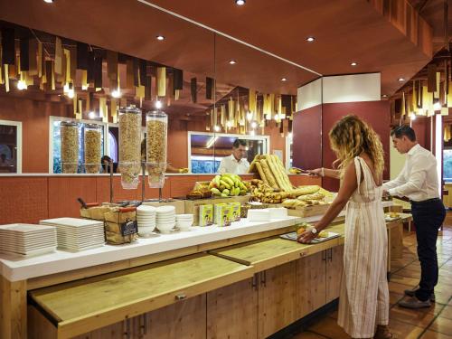 Un hombre y una mujer de pie en un mostrador de un restaurante. en ibis Thalassa Hyeres Plage, en Hyères