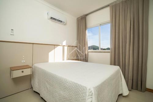 ein Schlafzimmer mit einem weißen Bett und einem großen Fenster in der Unterkunft Cobertura 07 Antares Bombinhas in Bombinhas