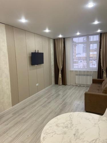 een woonkamer met een bank en een tv aan de muur bij Кокшебель Жк in Astana