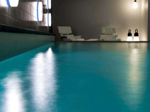 una piscina con sillas blancas en una habitación en Pullman Eindhoven Cocagne, en Eindhoven