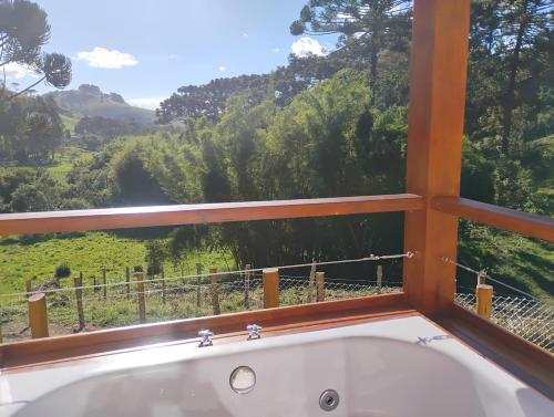 een badkuip in een kamer met een groot raam bij Chalé Topázio Gonçalves in Gonçalves