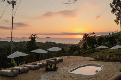 a sunset over the ocean with a pool and chairs and umbrellas at Mōmento Itamambuca in Ubatuba