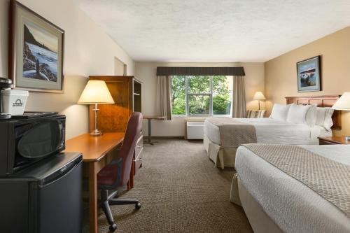 a hotel room with two beds and a desk with a television at Days Inn & Suites by Wyndham Moncton in Moncton