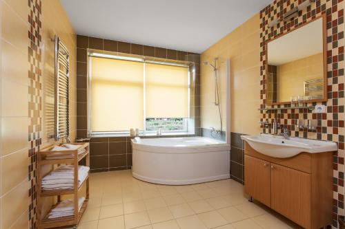baño con bañera, lavabo y ventana en Mineraliniai Apartamentai, en Druskininkai