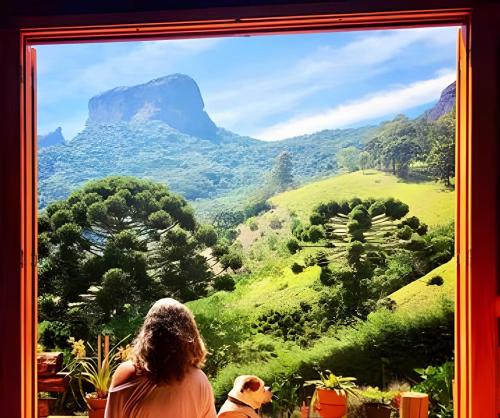 due persone che guardano fuori dalla finestra verso la vista sulle montagne di Casa Baú’au Vista Única Conforto em Familia a São Bento do Sapucaí