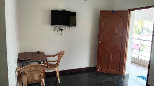 een kamer met een tafel en een televisie aan de muur bij Rainbow Guest House in Mahabalipuram