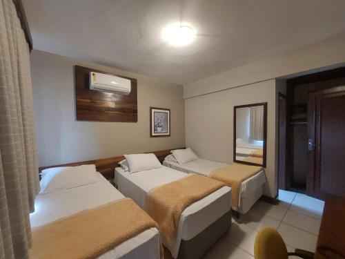 a hotel room with three beds and a mirror at Príncipe Hotel in Joinville