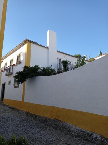 a white building with a fence next to a street at Casa das Glicínias in Óbidos