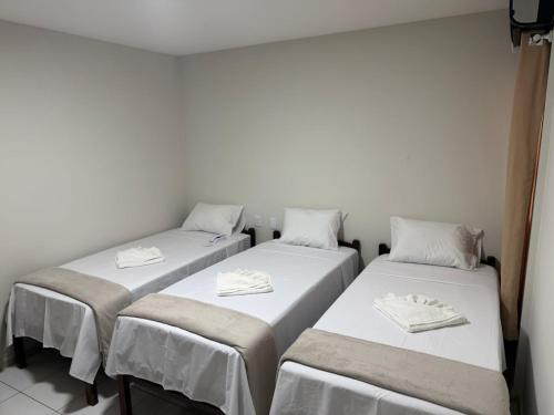 three beds in a room with white sheets and napkins at Hotel Portal do Sertao in Feira de Santana