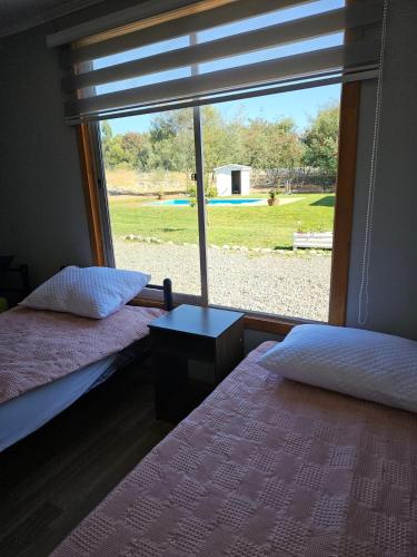 two beds in a room with a large window at Ribera del Ancoa in Llepu