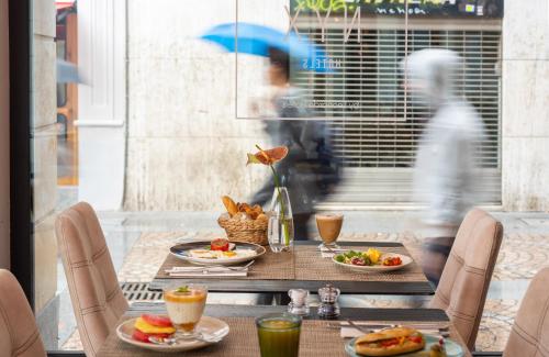 Una mesa con platos de comida y un hombre caminando junto a una ventana. en NYX Hotel Bilbao by Leonardo Hotels, en Bilbao