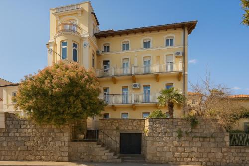 ein großes gelbes Gebäude hinter einer Steinmauer in der Unterkunft Blue Horizon Studio Opatija in Opatija