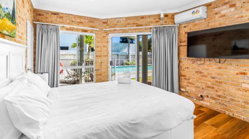 a bedroom with a white bed and a brick wall at Beachfront Escape in Forster