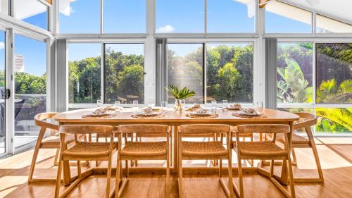 a dining room with a table and chairs and large windows at Beachfront Escape in Forster