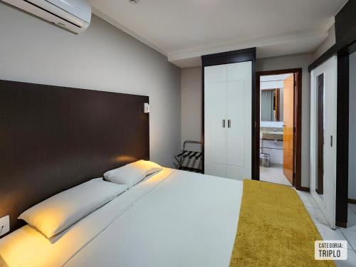 Un dormitorio con una gran cama blanca en una habitación. en Triângulo Apart Hotel, en Vitória