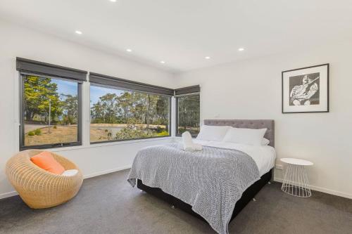 Un dormitorio con una cama y una silla y ventanas. en Sirocco on Main, en Merimbula