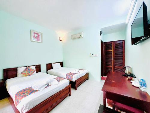a bedroom with two beds and a desk and a television at MUINE MOMO Homestay in Ấp Khánh Phước (1)