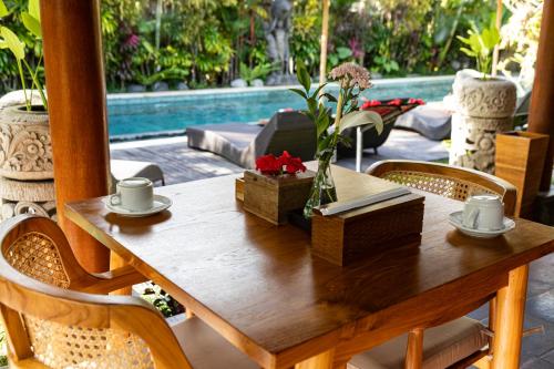 een houten tafel met bloemen op een terras met een zwembad bij The Runik Ubud in Ubud