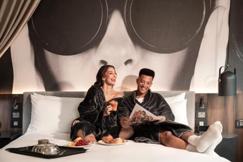 Un hombre y una mujer sentados en una cama con comida. en Hotel Indigo Melbourne on Flinders by IHG, en Melbourne