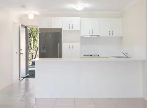 a white kitchen with white cabinets and a refrigerator at 20 Min to Brisbane, Walk to Train, Modern 2BR in Goodna