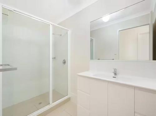 a white bathroom with a shower and a mirror at 20 Min to Brisbane, Walk to Train, Modern 2BR in Goodna