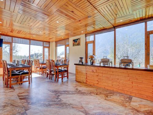 een eetkamer met tafels en stoelen en ramen bij Omavya Hotel Manali in Jagatsukh