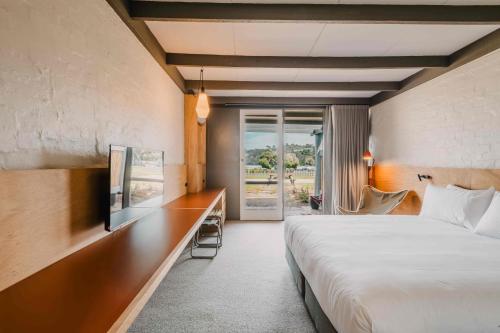 a bedroom with a bed and a desk with a television at The Black Dolphin Motel in Merimbula