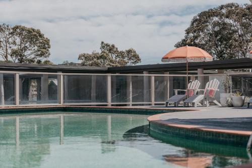 a swimming pool with two chairs and an umbrella at The Black Dolphin Motel in Merimbula