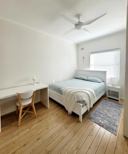 a white bedroom with a bed and a desk at Stunning Ground Floor Apt with Ocean Views in Cronulla