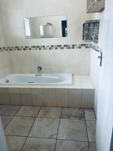 a bathroom with a tub with a sink and a mirror at La Bushka Guesthouse in Bela-Bela