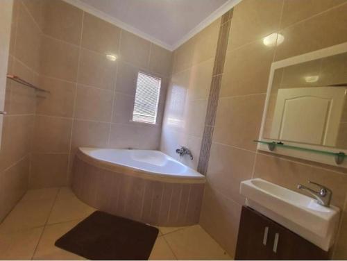 een badkamer met een bad, een wastafel en een spiegel bij Lovicc Guest house mafikeng in Mahikeng