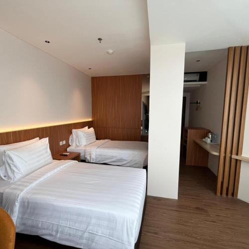 two beds in a hotel room with white sheets at WYNS Hotel Bandung in Bandung