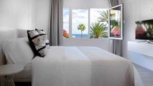 a white bedroom with a white bed and a window at Deva Beach Boutique Apartments in San Bartolomé