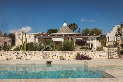 a swimming pool in front of a stone wall and a gazebo at Regina di Ulivi in Ostuni