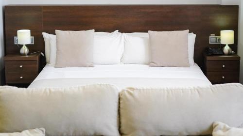 ein großes Bett mit weißen Kissen und einem Kopfteil aus Holz in der Unterkunft Le Grand Hôtel de Thiès in Thiès