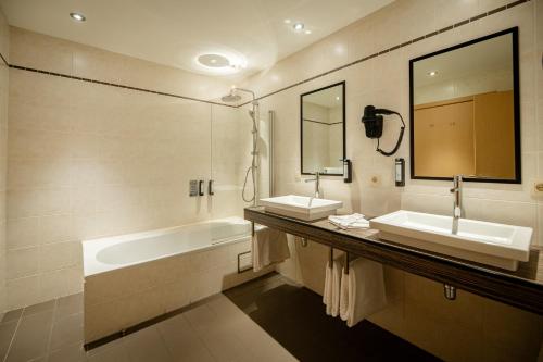 Un baño con dos lavabos, una bañera y un espejo. en Hotel-Restaurant Horizon Ath-Lessines, en Ghislenghien