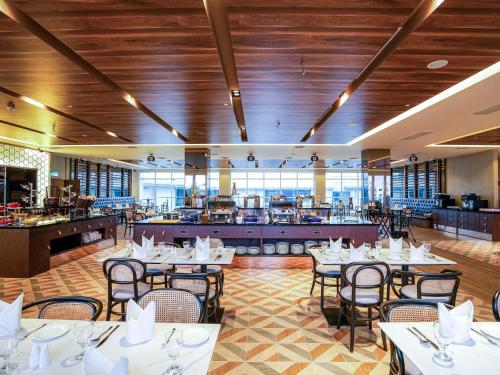 a dining room with tables and chairs and a kitchen at Mercure Langkawi Pantai Cenang in Pantai Cenang