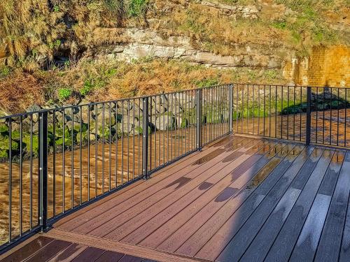 a wooden deck with a fence on top of a cliff at Pilot Me Cottage in Staithes