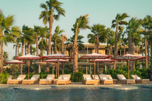 een zwembad met stoelen, parasols en palmbomen bij SLS The Red Sea in Ḩanak