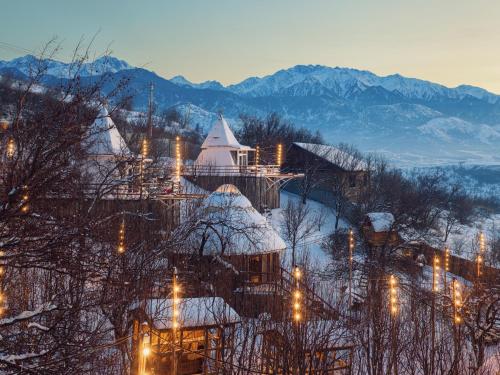 een groep gebouwen op een besneeuwde heuvel met verlichting bij Pik Talgar Eco Village in Talghar