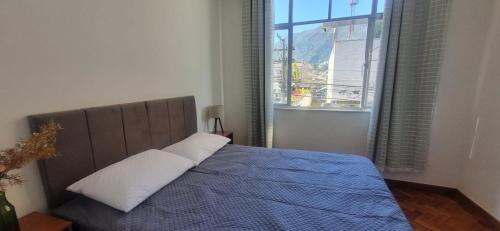 a bedroom with a bed with a blue blanket and a window at O melhor de Terê in Teresópolis