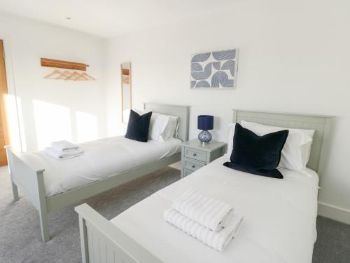 two beds in a room with white walls and blue pillows at Glynllifon 4 in Llanallgo