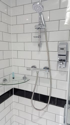 La salle de bains est pourvue d'une douche avec un tuyau et de carrelage blanc. dans l'établissement Rye Court Hotel, à High Wycombe