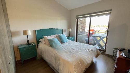 a bedroom with a bed with blue pillows and a balcony at Departamento Costa Pucón in El Cerrillo