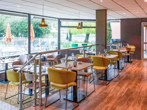 Un restaurante con mesas, sillas y ventanas. en Novotel Metz Amnéville, en Maizières-lès-Metz