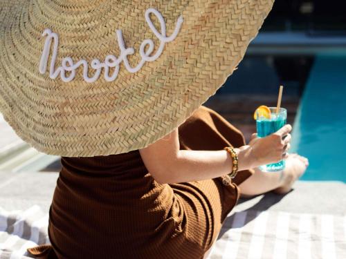 a woman wearing a straw hat sitting next to a pool at Novotel Montpellier in Montpellier
