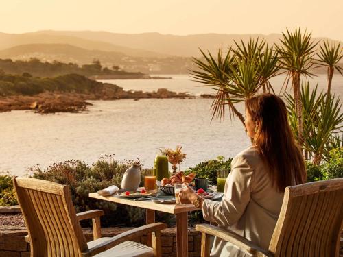 a woman sitting at a table with a meal on it at Sofitel Golfe d'Ajaccio Thalassa Sea & Spa in Ajaccio