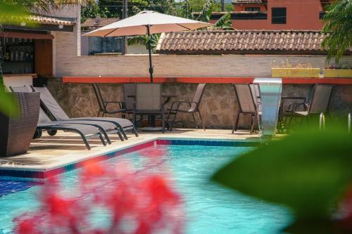 a swimming pool with a table and chairs and an umbrella at VELINN Pousada Face Norte in Ilhabela